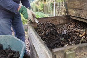 Une personne portant des gants utilise une fourche de jardin pour retourner le compost